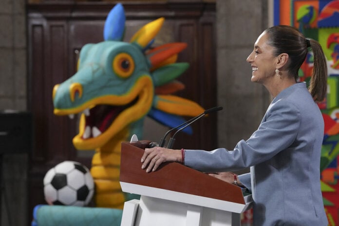 Sheinbaum at a press conference podium in front of a cartoon dragon or maybe quetzalcoatl with a soccer ball
