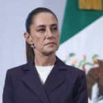 President Claudia Sheinbaum stands in front of a Mexican flag