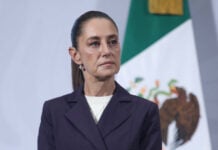 President Claudia Sheinbaum stands in front of a Mexican flag