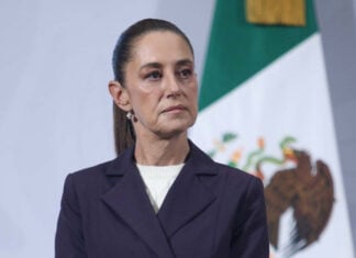 President Claudia Sheinbaum stands in front of a Mexican flag