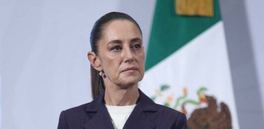 President Claudia Sheinbaum stands in front of a Mexican flag