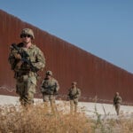 US soldiers walk along a rust-colored Mexico border wall
