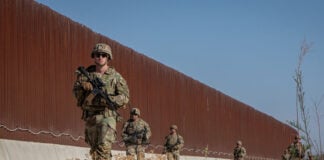 US soldiers walk along a rust-colored Mexico border wall