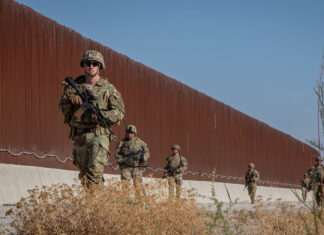 US soldiers walk along a rust-colored Mexico border wall