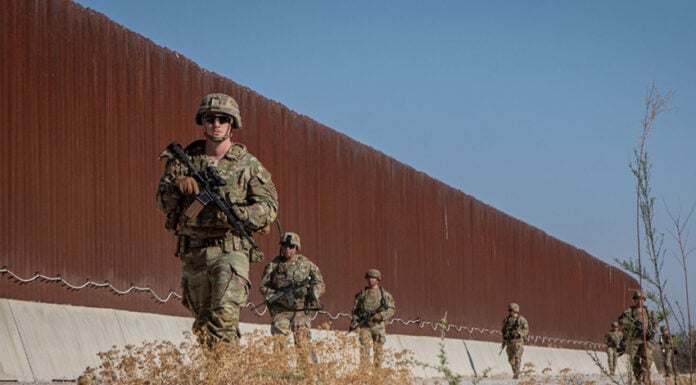 US soldiers walk along a rust-colored Mexico border wall