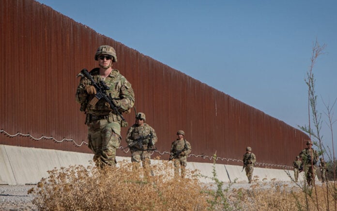 US soldiers walk along a rust-colored Mexico border wall