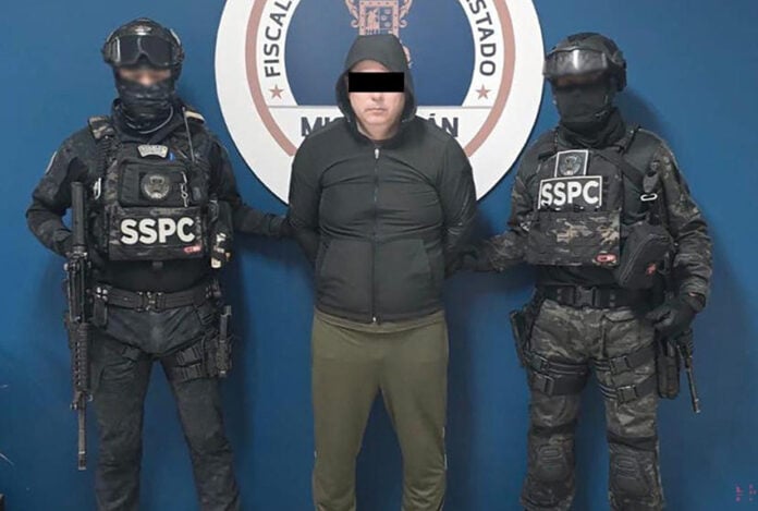 A detained man wearing a hoodie stands next to two uniformed SSPC agents.