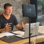 Travis Bembenek sits at a desk recording a podcast while wearing a Mexico News Daily T-shirt