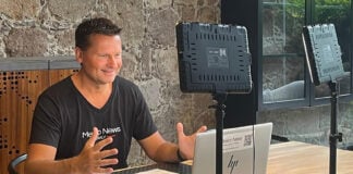 Travis Bembenek sits at a desk recording a podcast while wearing a Mexico News Daily T-shirt