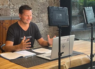 Travis Bembenek sits at a desk recording a podcast while wearing a Mexico News Daily T-shirt