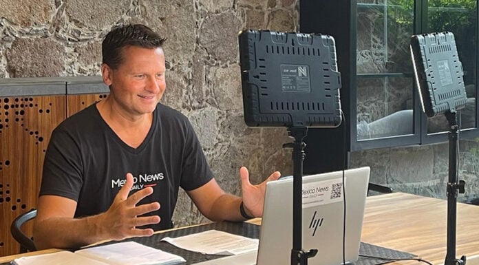 Travis Bembenek sits at a desk recording a podcast while wearing a Mexico News Daily T-shirt
