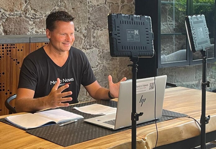 Travis Bembenek sits at a desk recording a podcast while wearing a Mexico News Daily T-shirt