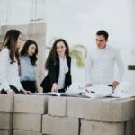 A team of architects and engineers reviews blueprints on a stack of concrete blocks at a home building construction site in Mexico.
