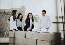 A team of architects and engineers reviews blueprints on a stack of concrete blocks at a home building construction site in Mexico.