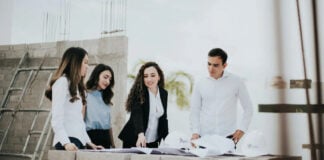 A team of architects and engineers reviews blueprints on a stack of concrete blocks at a home building construction site in Mexico.