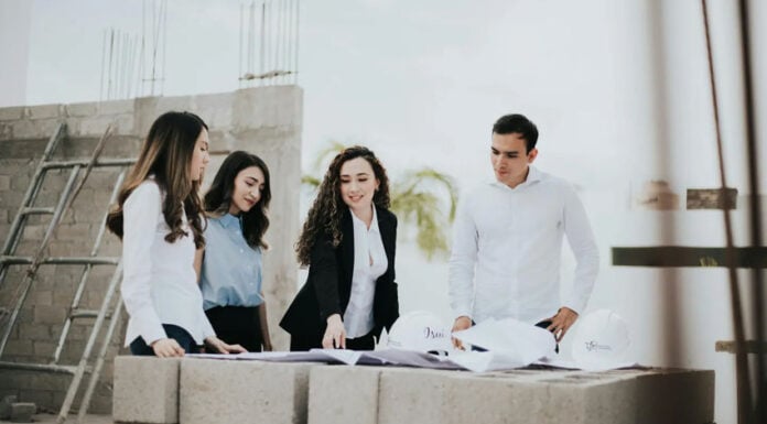 A team of architects and engineers reviews blueprints on a stack of concrete blocks at a home building construction site in Mexico.