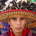 Close-up portrait of a Wixárika man wearing a traditional hat adorned with feathers and intricate beadwork