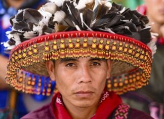 Close-up portrait of a Wixárika man wearing a traditional hat adorned with feathers and intricate beadwork