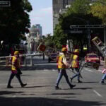 Workers in neon vests cross Avenida Juárez in Mexico City carrying ladders