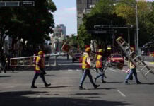 Workers in neon vests cross Avenida Juárez in Mexico City carrying ladders