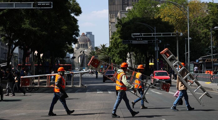 Workers in neon vests cross Avenida Juárez in Mexico City carrying ladders