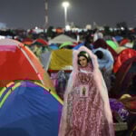 A Virgin of Guadalupe figure in sparkling pink robes watches over a plaza filled with colorful camping tents