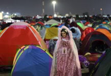 A Virgin of Guadalupe figure in sparkling pink robes watches over a plaza filled with colorful camping tents