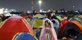 A Virgin of Guadalupe figure in sparkling pink robes watches over a plaza filled with colorful camping tents