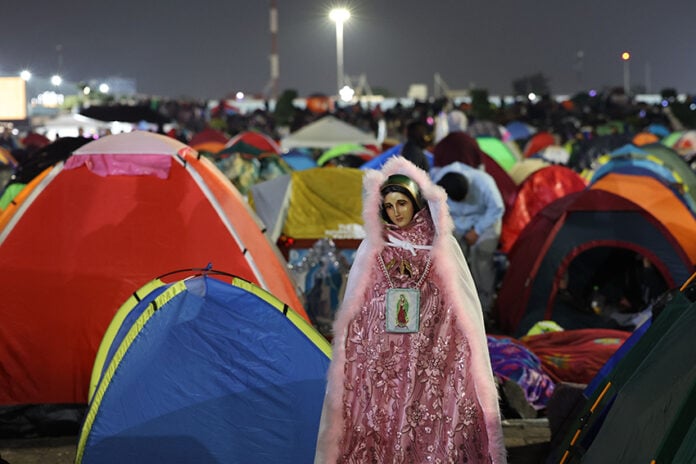 A Virgin of Guadalupe figure in sparkling pink robes watches over a plaza filled with colorful camping tents