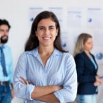 Mexican woman smiles at the camera in front of a group of coworkers all in business casual attire