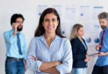 Mexican woman smiles at the camera in front of a group of coworkers all in business casual attire