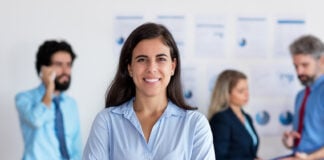Mexican woman smiles at the camera in front of a group of coworkers all in business casual attire