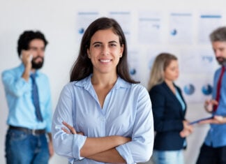 Mexican woman smiles at the camera in front of a group of coworkers all in business casual attire