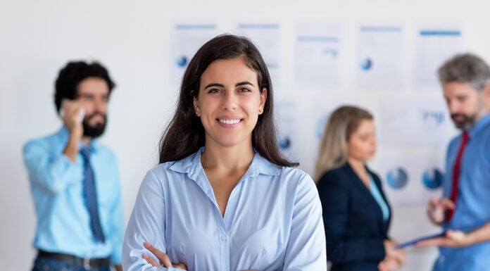 Mexican woman smiles at the camera in front of a group of coworkers all in business casual attire