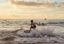"A young boy skimboarding on a wave during a golden sunset, illustrating the active coastal lifestyle featured in Puerto Vallarta community news December 2025."