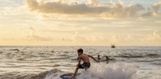 "A young boy skimboarding on a wave during a golden sunset, illustrating the active coastal lifestyle featured in Puerto Vallarta community news December 2025."