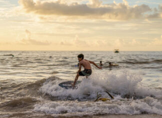 "A young boy skimboarding on a wave during a golden sunset, illustrating the active coastal lifestyle featured in Puerto Vallarta community news December 2025."