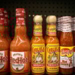 Bottles of different brands of hot sauces on a supermarket shelf.