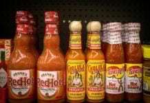 Bottles of different brands of hot sauces on a supermarket shelf.
