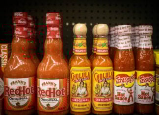 Bottles of different brands of hot sauces on a supermarket shelf.