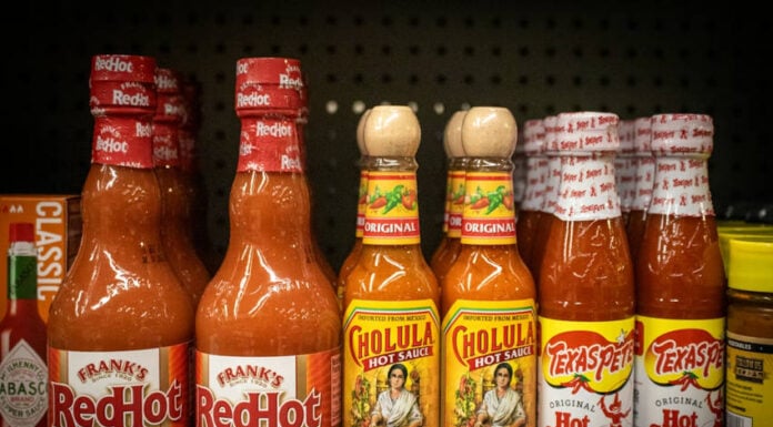 Bottles of different brands of hot sauces on a supermarket shelf.