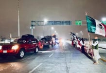Government agents wave Mexican flags as a caravan of cars drives down a highway at night