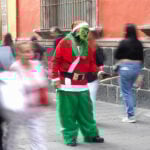 An organ grinder in a grinch costumes holds out his hat for coins on a street of Mexico City