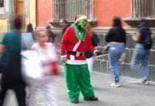 An organ grinder in a grinch costumes holds out his hat for coins on a street of Mexico City