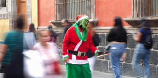 An organ grinder in a grinch costumes holds out his hat for coins on a street of Mexico City