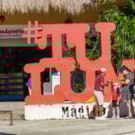A family takes photos near a sculpture of the word #TULUM