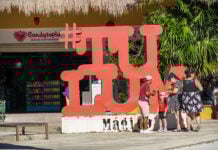 A family takes photos near a sculpture of the word #TULUM