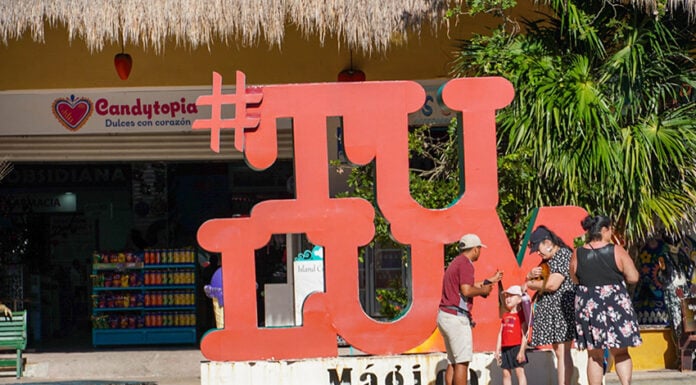 A family takes photos near a sculpture of the word #TULUM