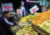 A customer selects fruit in a market with prices displayed in Mexican pesos