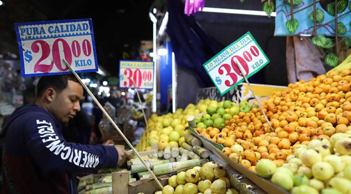 A customer selects fruit in a market with prices displayed in Mexican pesos